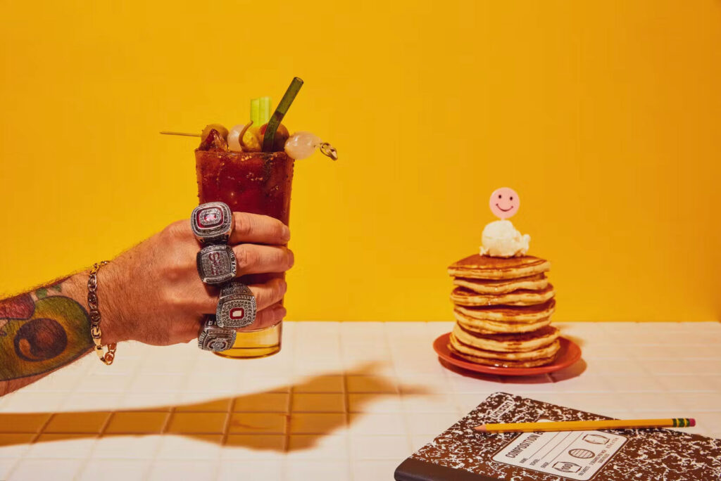 HangOverEasy Brunch, hand holding a Bloody Mary next to a delicious stack of pancakes